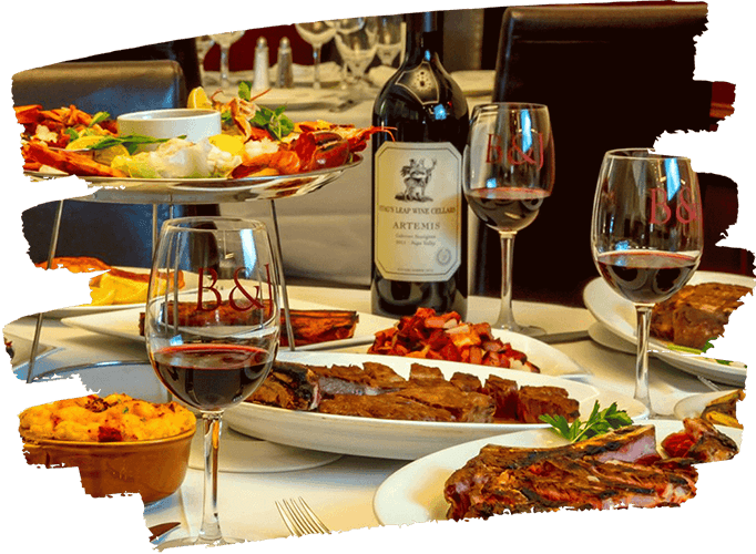 Table set with plates of grilled steak, seafood platter, wine glasses filled with red wine, and a bottle of Artemis wine.