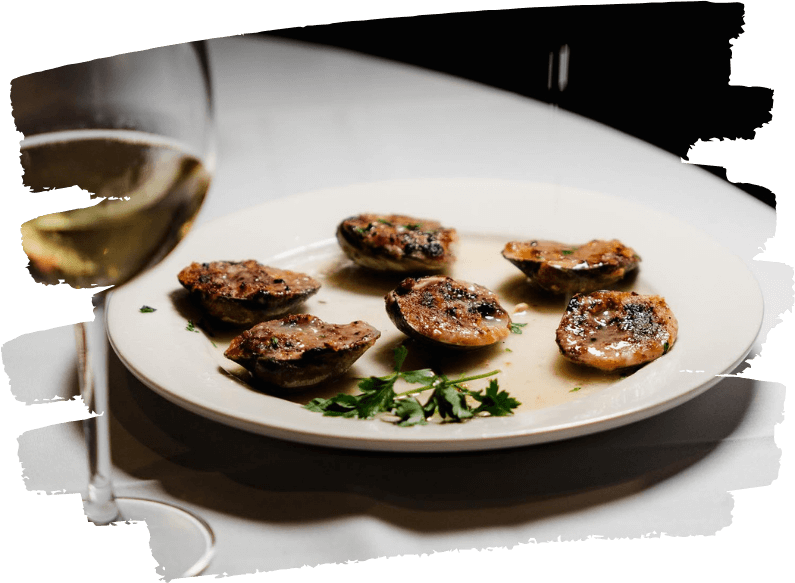 Plate of clams oreganata served with white wine and fresh parsley garnish on a white tablecloth, photographed under warm lighting